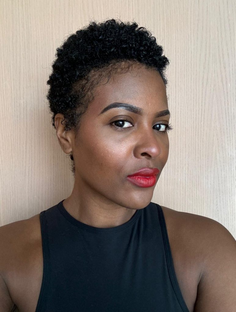 A profile shot of a black female wearing a short sleeved black top with red lipstick and short hair