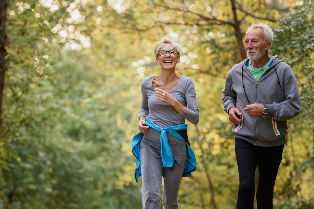 Cheerful active senior couple jogging in the park. Exercise toge