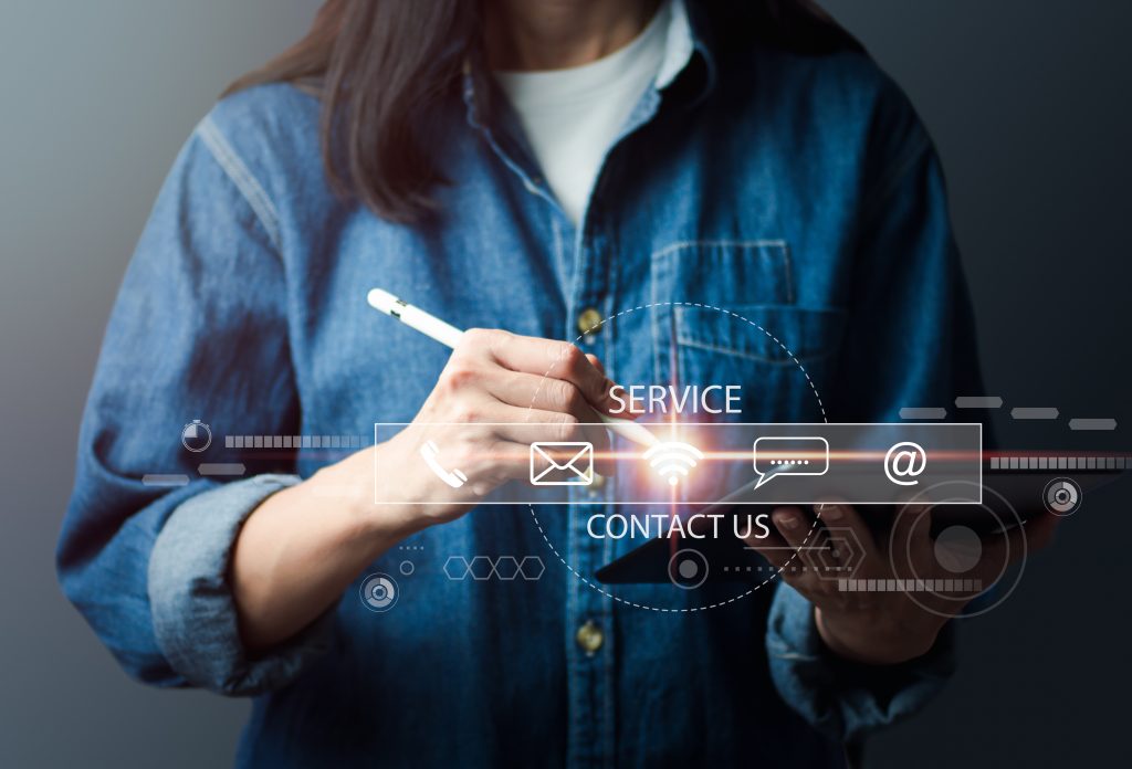The woman in jeans is using a digital tablet and interacting with virtual contact icons on the screen ( email, address, live chat, internet wifi ). Contact us or call our customer service hotline.