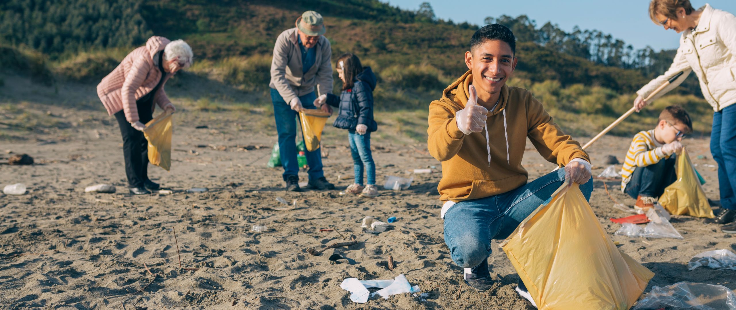 Young man picking up trash with group of volunteers on the beach