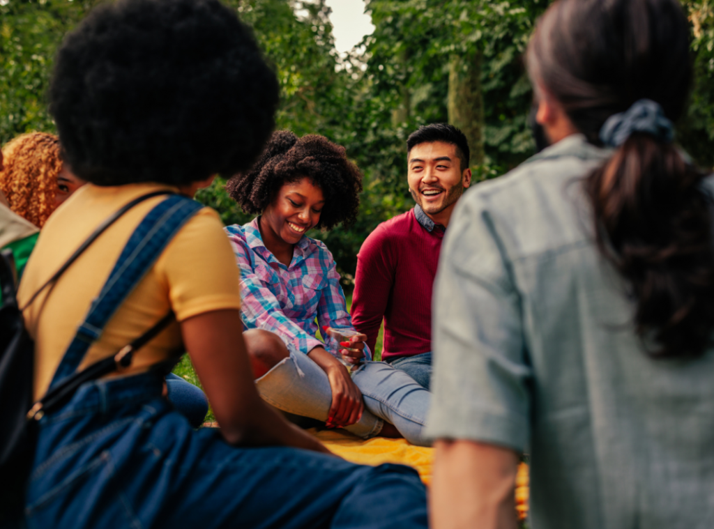 Two black women and an Oreintal man sitting in the park on the grass