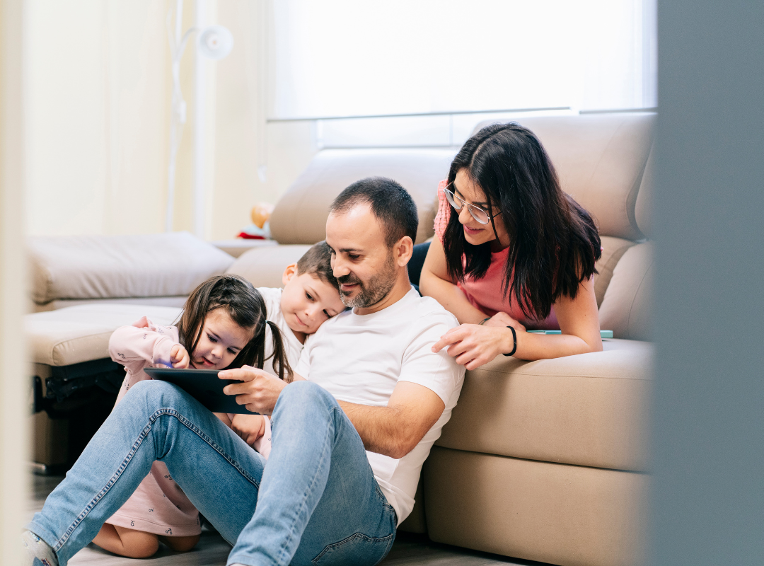 A single father holding a tablet as three children watching on