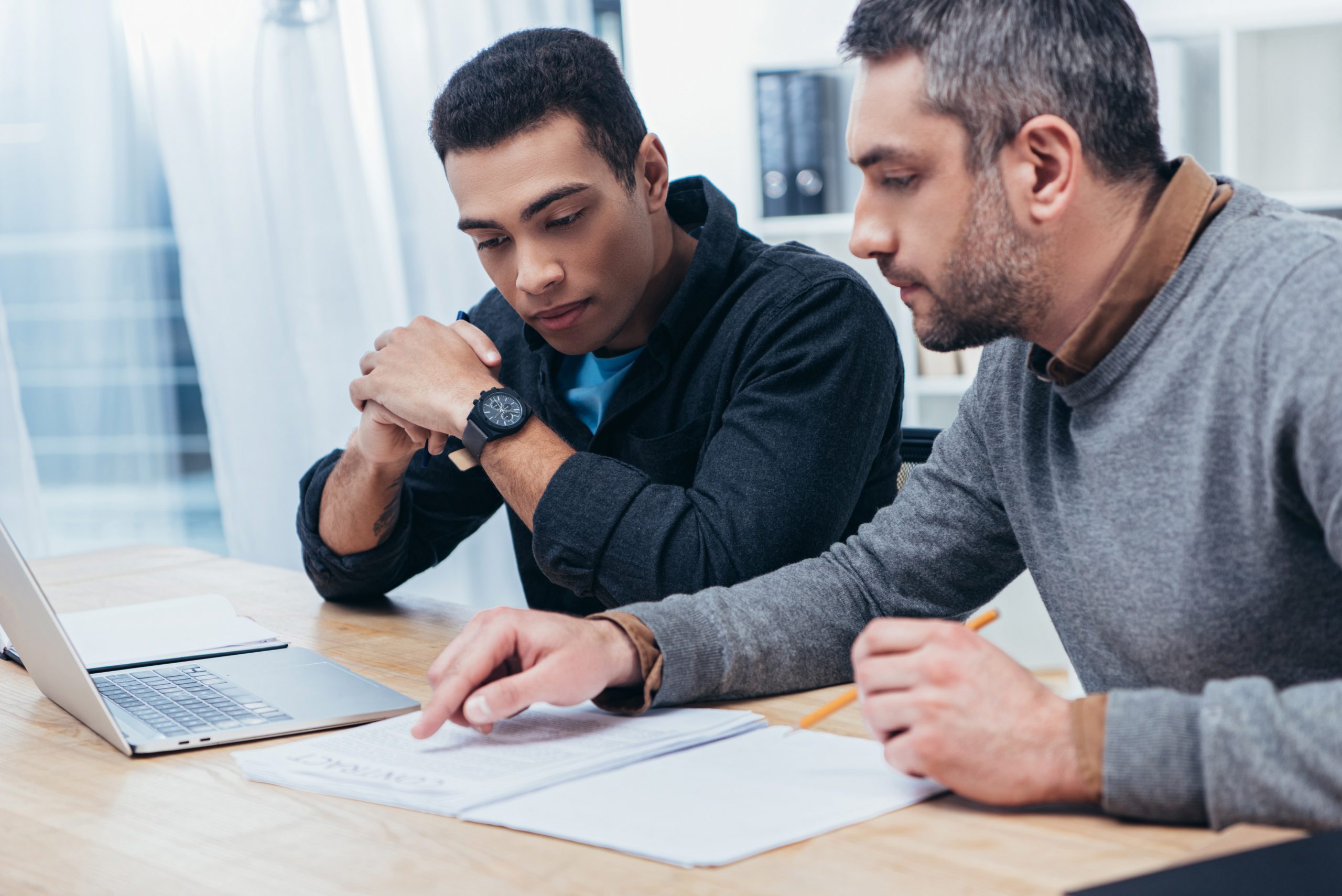 concentrated male coworkers using laptop and working with papers