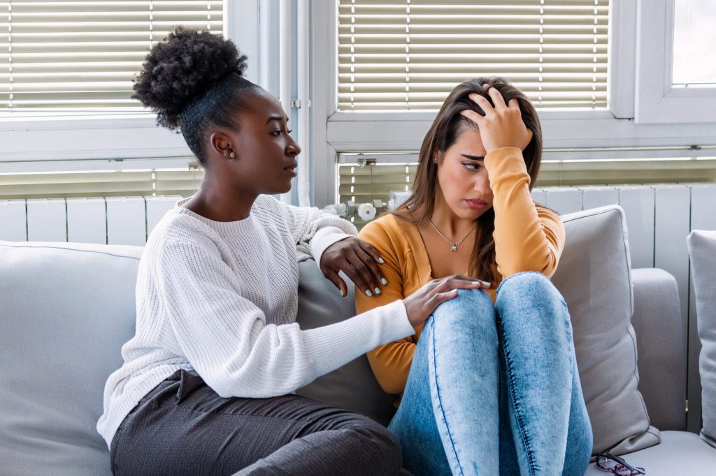 Woman hugging her depressed friend at home, closeup. Young girl supporting her crying girlfriend.