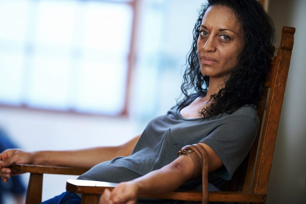 Portrait of a drug addict sitting in a chair with a belt around her arm.