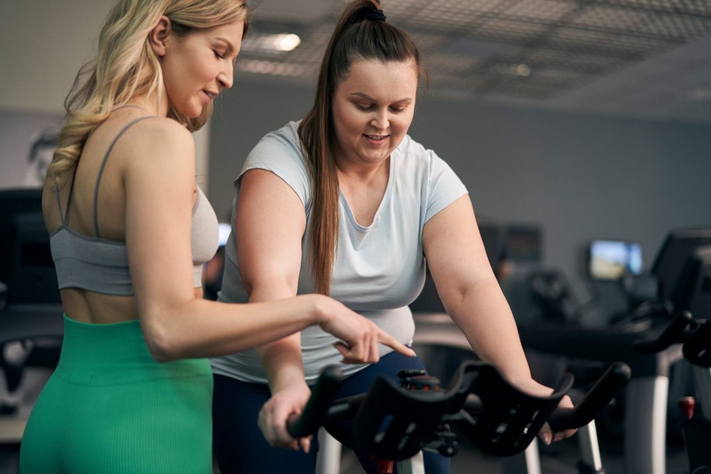 Caucasian instructor helping plus size woman at the gym