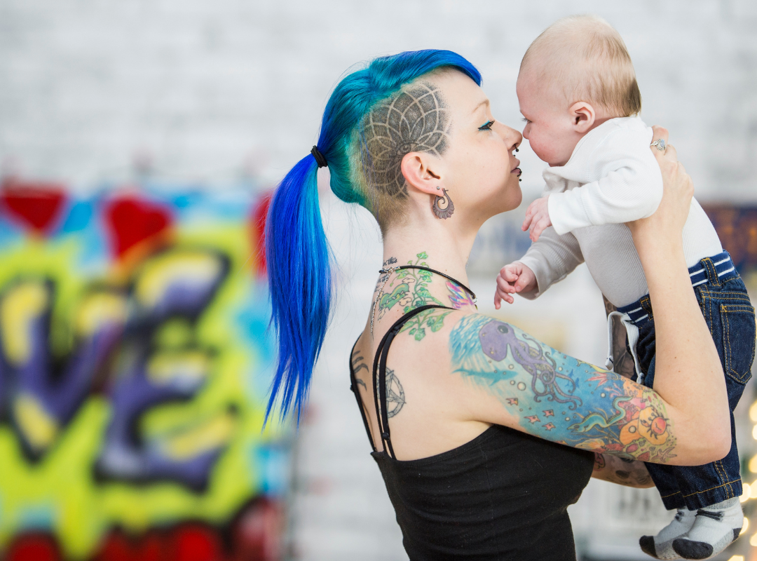 Single mother with tattoo's and bright blue hair kissing her baby